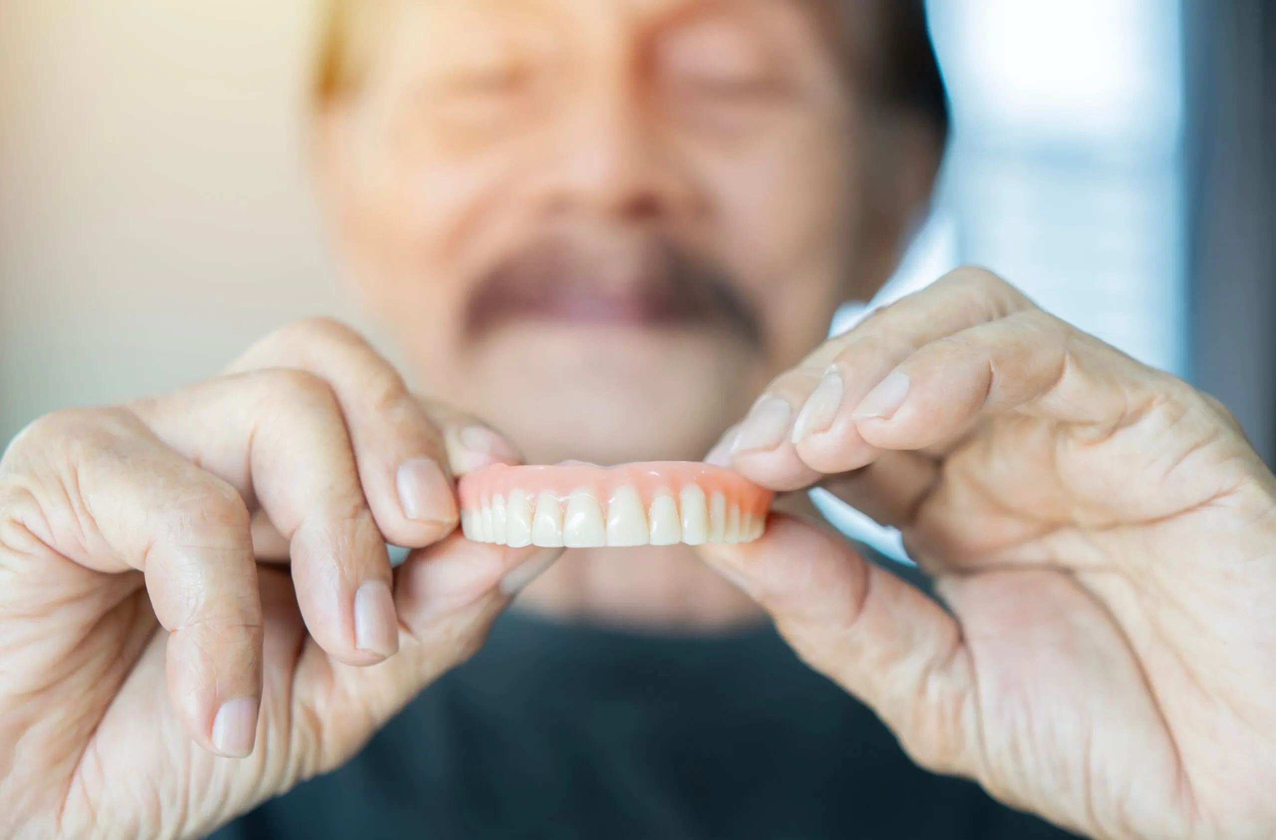 senior man holding up his dentures confidently