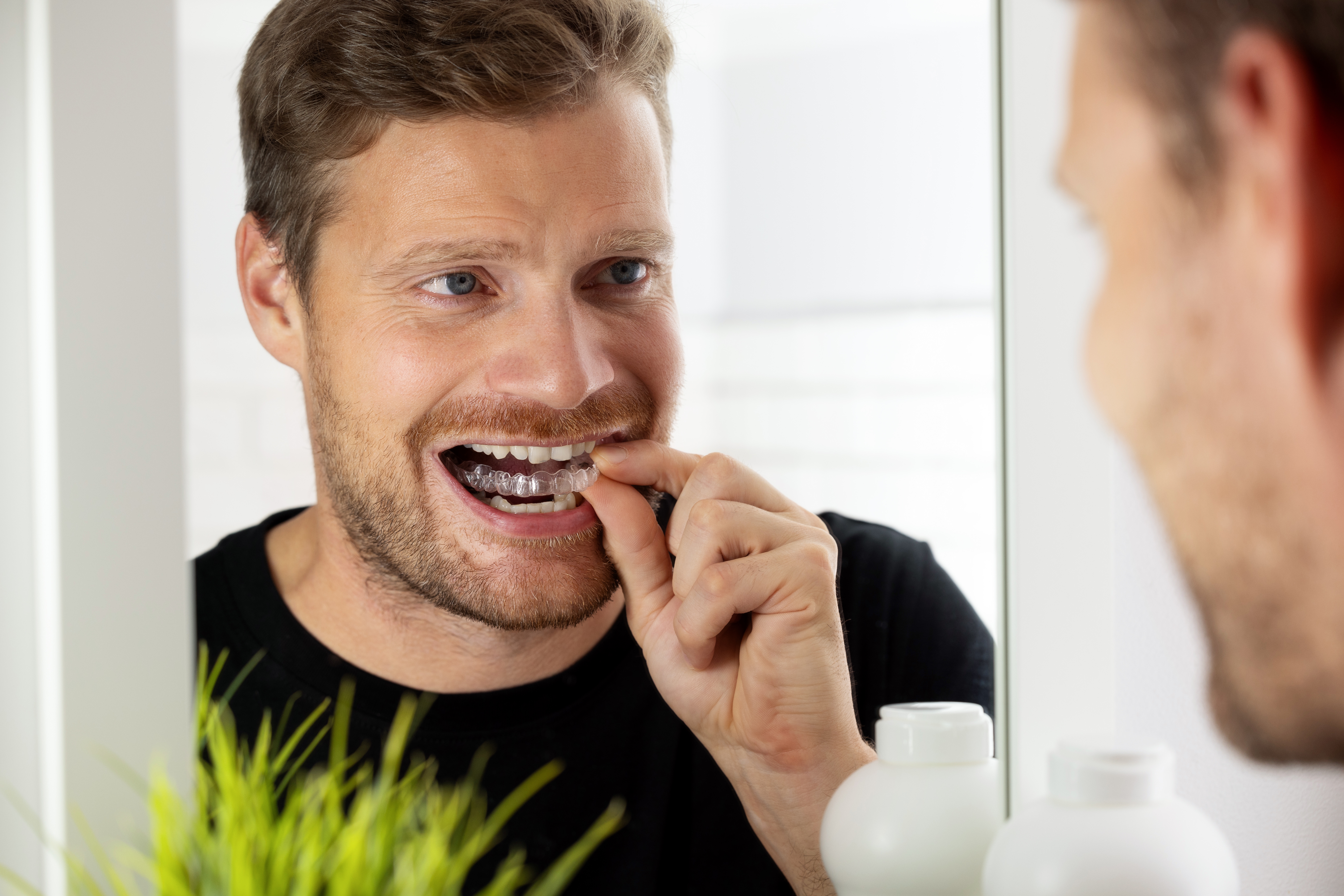 adult man inserting his clear aligners looking at mirror