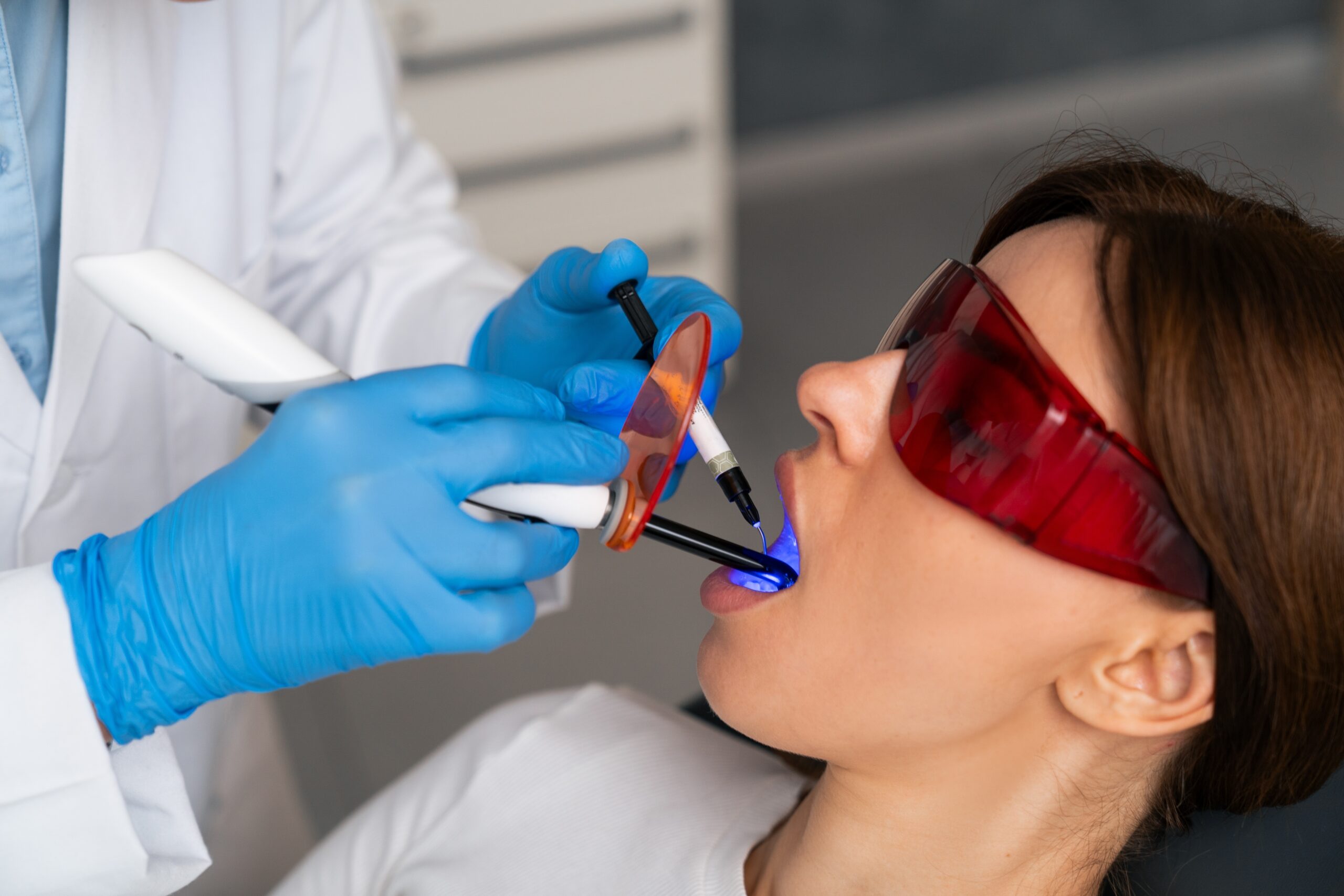 dentist in blue gloves using a dental laser to treat female patient
