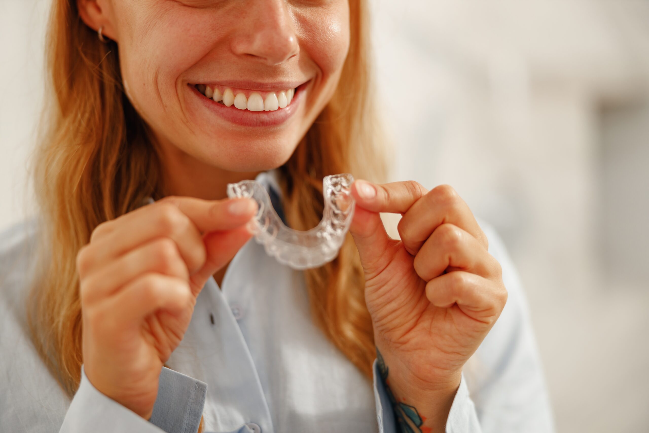 A cheerful woman holds up her clear dental aligner, proudly showing off her confident and radiant smile